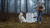 White dog with their white collapsible crate in the forest