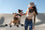 two dogs sitting on top of a white collapsible dog crate, while their mom pets them. In the background are sand dunes